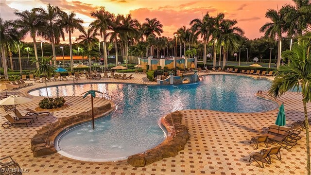 pool at dusk with pool water feature and a patio