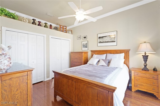 bedroom featuring ornamental molding, two closets, ceiling fan, and dark wood-type flooring