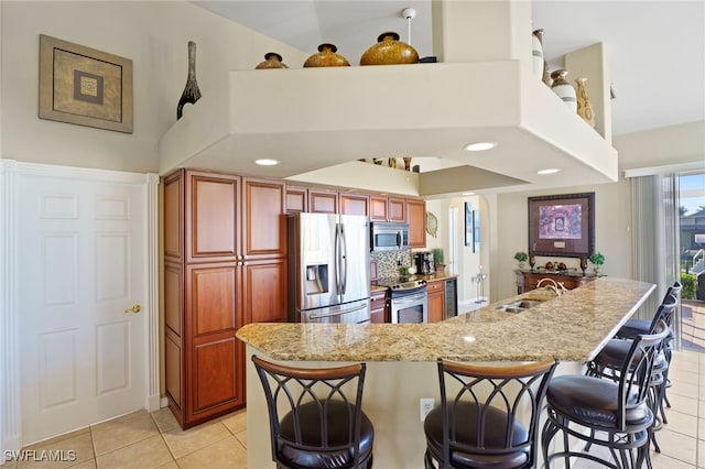 kitchen featuring light stone countertops, appliances with stainless steel finishes, sink, a breakfast bar area, and light tile patterned flooring