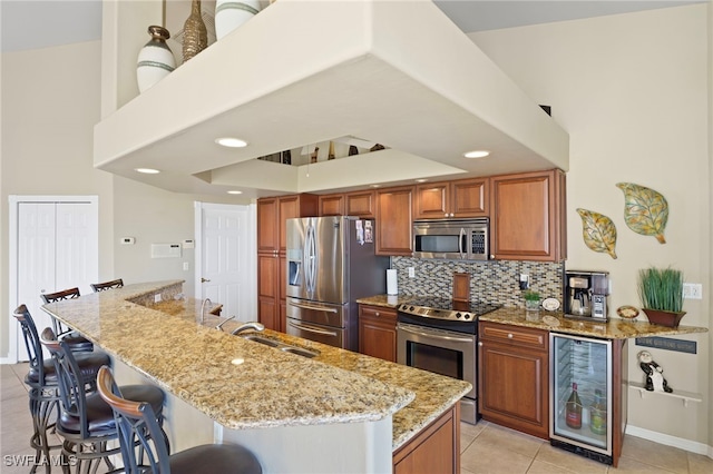 kitchen with sink, stainless steel appliances, wine cooler, light stone counters, and a breakfast bar