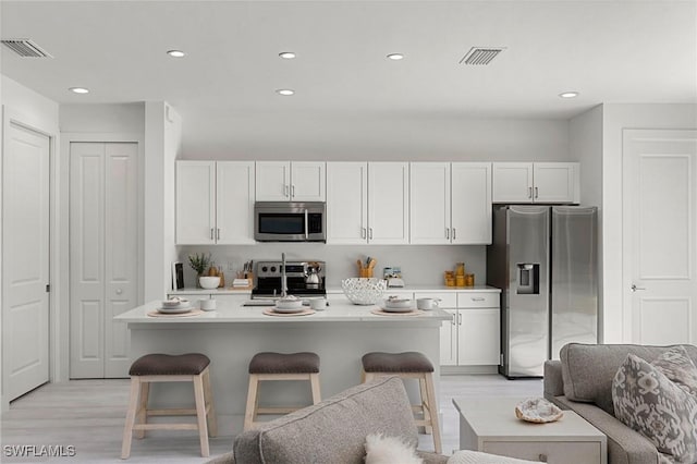 kitchen with a kitchen island with sink, white cabinets, light hardwood / wood-style flooring, appliances with stainless steel finishes, and a breakfast bar area