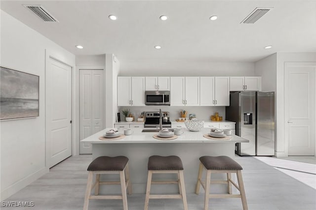 kitchen with a kitchen breakfast bar, stainless steel appliances, white cabinetry, and a kitchen island with sink