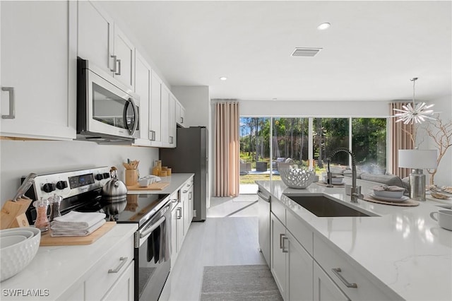 kitchen featuring light stone countertops, stainless steel appliances, sink, pendant lighting, and white cabinets