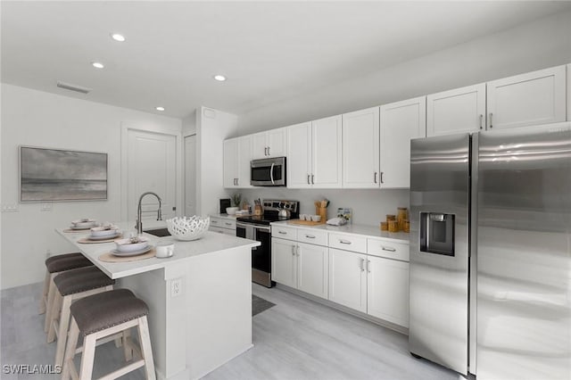 kitchen featuring a kitchen bar, appliances with stainless steel finishes, white cabinetry, and a kitchen island with sink