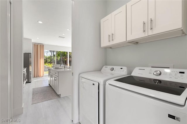 clothes washing area featuring cabinets, light wood-type flooring, sink, and washing machine and clothes dryer