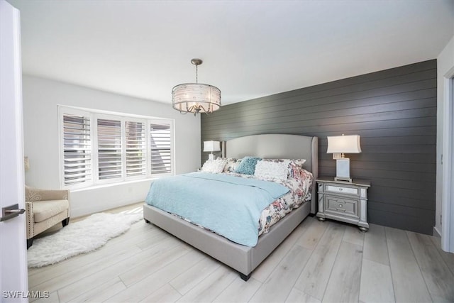 bedroom featuring wood walls, light hardwood / wood-style floors, and an inviting chandelier