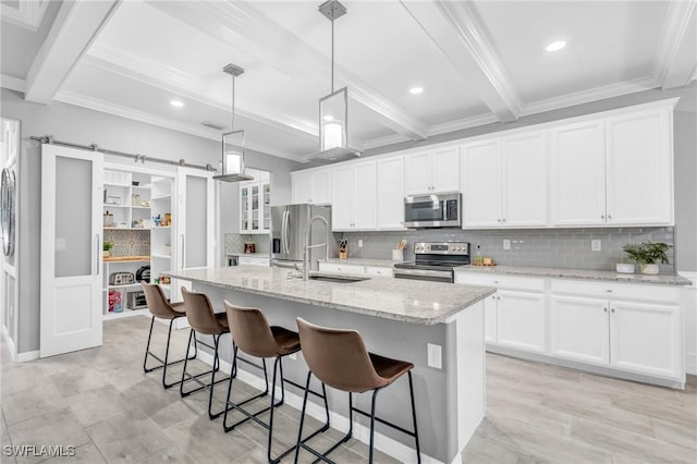 kitchen featuring stainless steel appliances, a barn door, a center island with sink, white cabinets, and hanging light fixtures