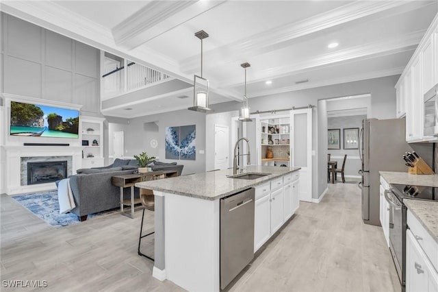 kitchen featuring light stone countertops, appliances with stainless steel finishes, a kitchen island with sink, sink, and white cabinetry