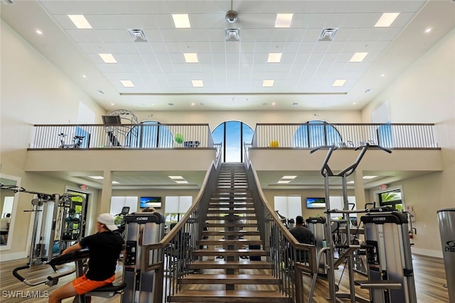 exercise room featuring wood-type flooring, a towering ceiling, and a drop ceiling