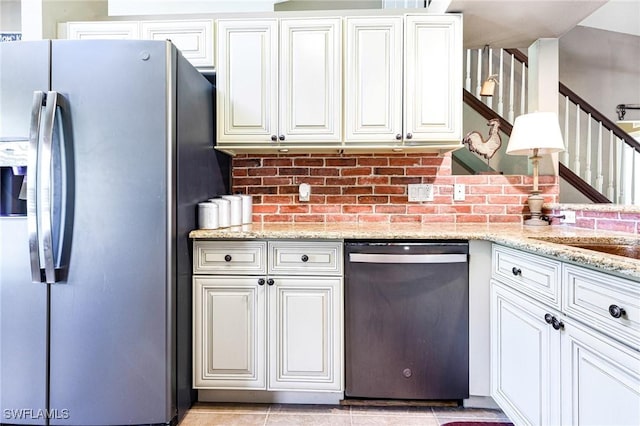 kitchen featuring appliances with stainless steel finishes, light tile patterned floors, white cabinets, and light stone counters