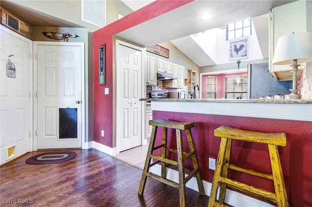 kitchen featuring white cabinetry, a kitchen breakfast bar, light hardwood / wood-style floors, and vaulted ceiling