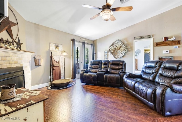 living room with a brick fireplace, dark wood-type flooring, and ceiling fan