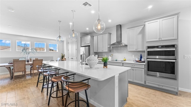 kitchen featuring pendant lighting, a breakfast bar, a kitchen island with sink, wall chimney exhaust hood, and appliances with stainless steel finishes