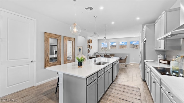 kitchen with sink, wall chimney exhaust hood, an island with sink, pendant lighting, and a breakfast bar