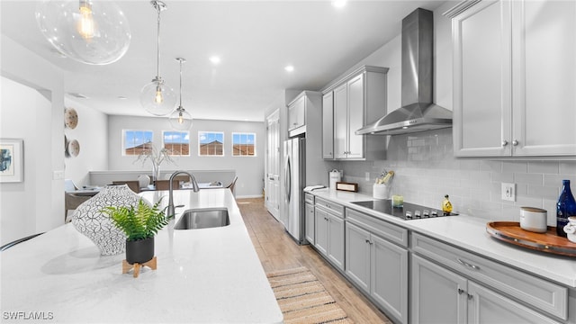 kitchen with decorative backsplash, stainless steel fridge, black electric stovetop, wall chimney exhaust hood, and sink