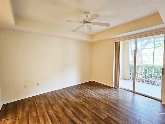 empty room with ceiling fan, dark hardwood / wood-style flooring, and a raised ceiling