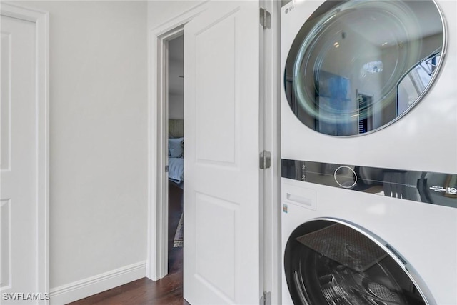 laundry room with dark wood-style floors, laundry area, stacked washer / drying machine, and baseboards