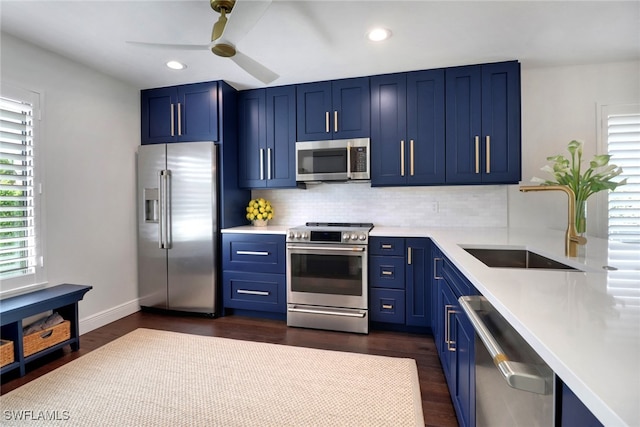 kitchen featuring blue cabinetry, light countertops, decorative backsplash, appliances with stainless steel finishes, and a sink