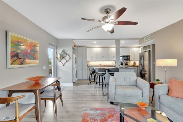 living room featuring ceiling fan, light wood-type flooring, and stacked washing maching and dryer