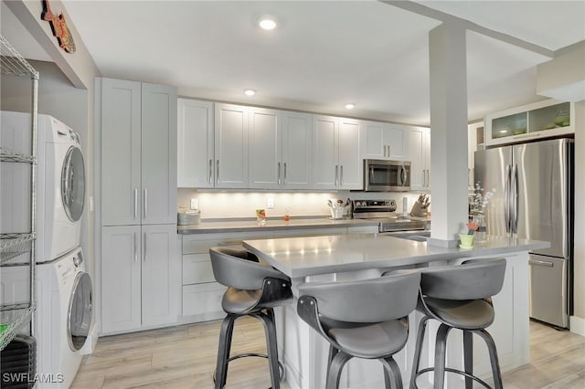 kitchen featuring light hardwood / wood-style flooring, stacked washer / dryer, a breakfast bar, white cabinets, and appliances with stainless steel finishes