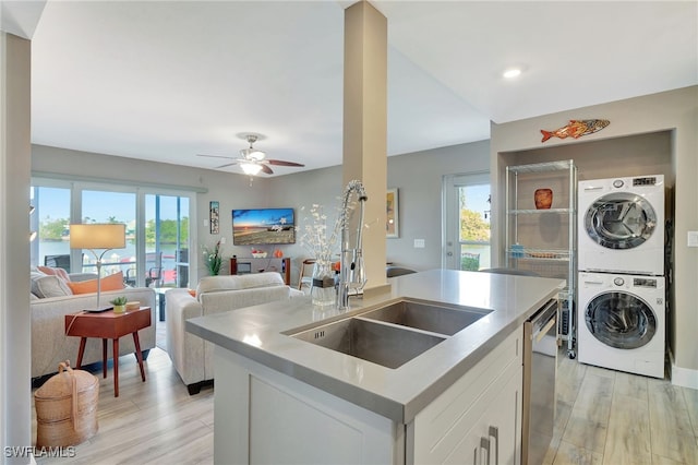 kitchen featuring light wood-type flooring, stainless steel dishwasher, sink, white cabinetry, and stacked washer / drying machine