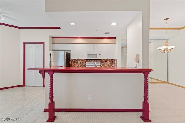 kitchen with hanging light fixtures, stove, white microwave, freestanding refrigerator, and white cabinets