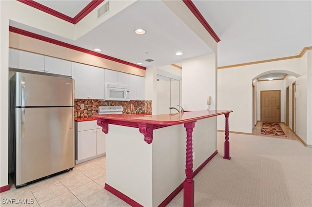 kitchen with white microwave, a breakfast bar, white cabinets, freestanding refrigerator, and an island with sink