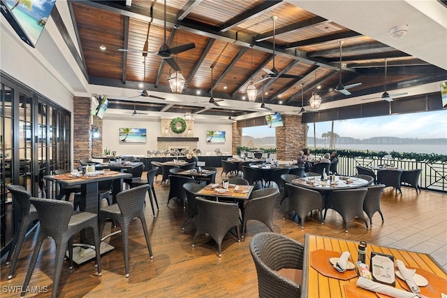 dining area featuring a ceiling fan, lofted ceiling with beams, wooden ceiling, wood finished floors, and a fireplace