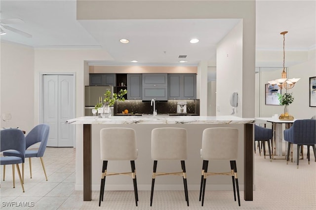 kitchen with decorative backsplash, stainless steel refrigerator, a kitchen breakfast bar, light stone countertops, and gray cabinets