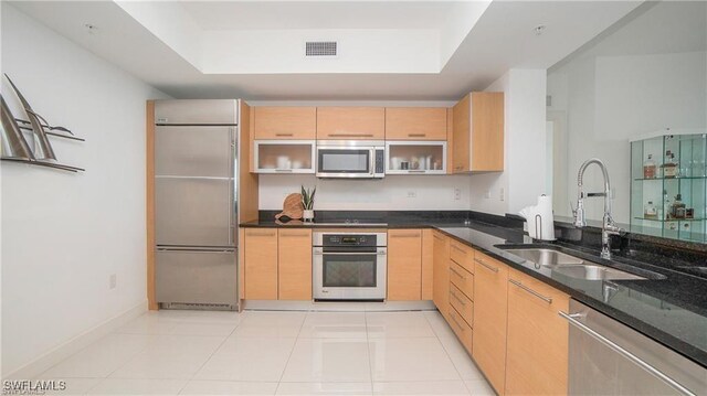 kitchen with dark stone counters, sink, light tile patterned floors, light brown cabinetry, and appliances with stainless steel finishes