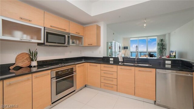 kitchen with light brown cabinetry, sink, dark stone counters, and appliances with stainless steel finishes