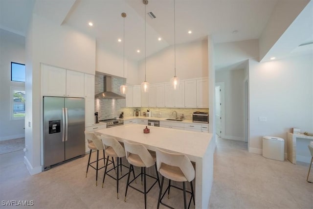 kitchen with pendant lighting, high vaulted ceiling, wall chimney range hood, appliances with stainless steel finishes, and white cabinetry