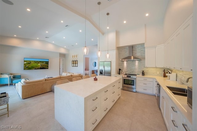 kitchen with white cabinetry, sink, stainless steel appliances, wall chimney range hood, and a kitchen island