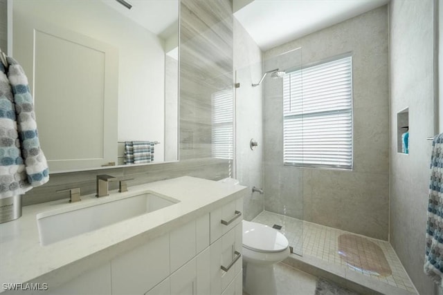 bathroom featuring a tile shower, vanity, toilet, and plenty of natural light