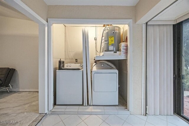 laundry room with electric water heater, washing machine and clothes dryer, and light tile patterned floors