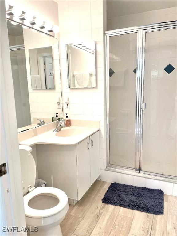 bathroom with vanity, toilet, wood-type flooring, and a shower with door