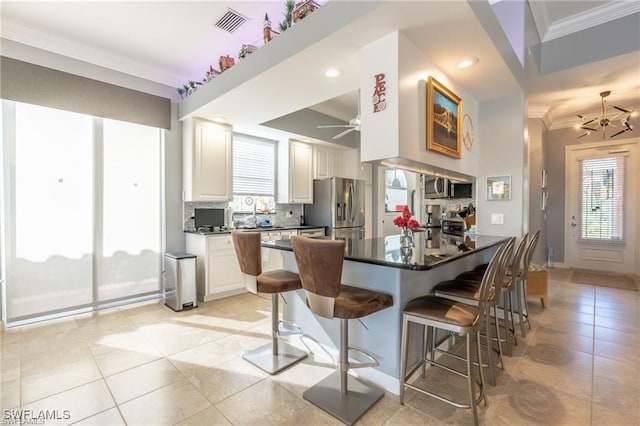 kitchen with white cabinetry, a kitchen bar, decorative backsplash, kitchen peninsula, and stainless steel appliances