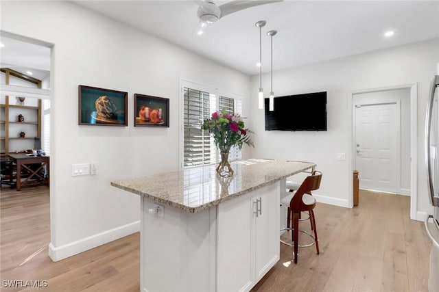 kitchen featuring light hardwood / wood-style flooring, white cabinetry, hanging light fixtures, light stone counters, and a kitchen island