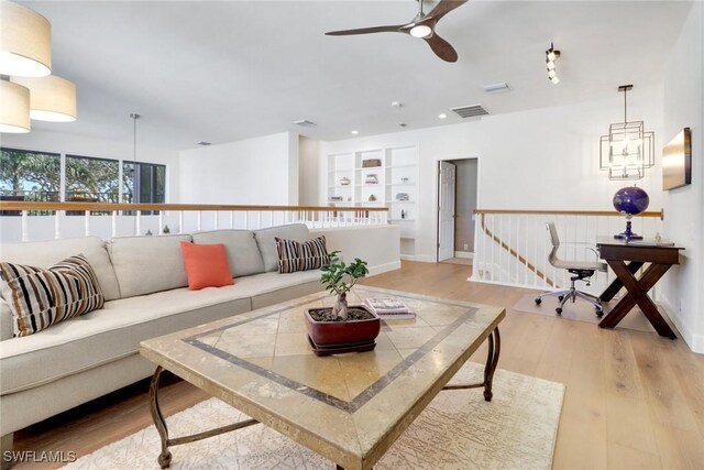 living room featuring ceiling fan, light wood-type flooring, and built in shelves