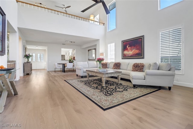 living room with ceiling fan, light hardwood / wood-style floors, and a towering ceiling