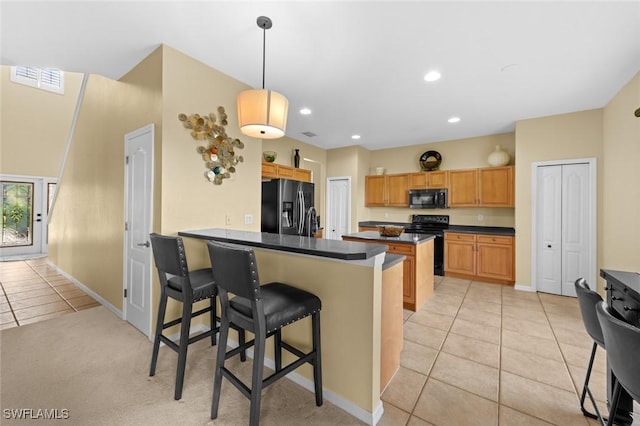 kitchen with black appliances, light tile patterned floors, decorative light fixtures, kitchen peninsula, and a breakfast bar area