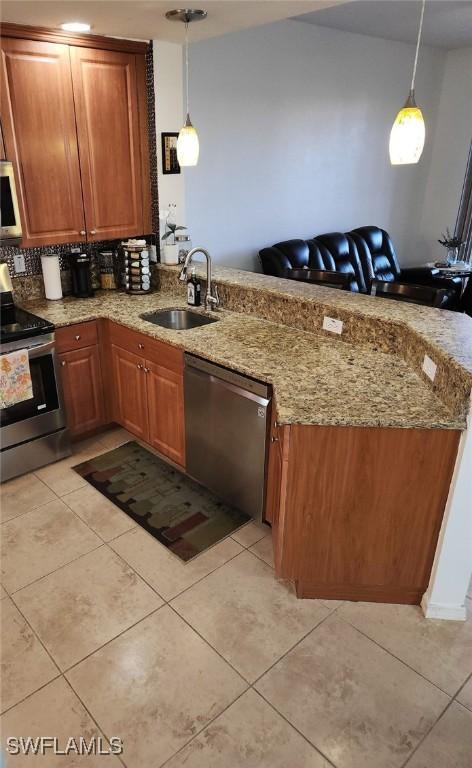 kitchen with sink, appliances with stainless steel finishes, decorative light fixtures, light stone counters, and kitchen peninsula