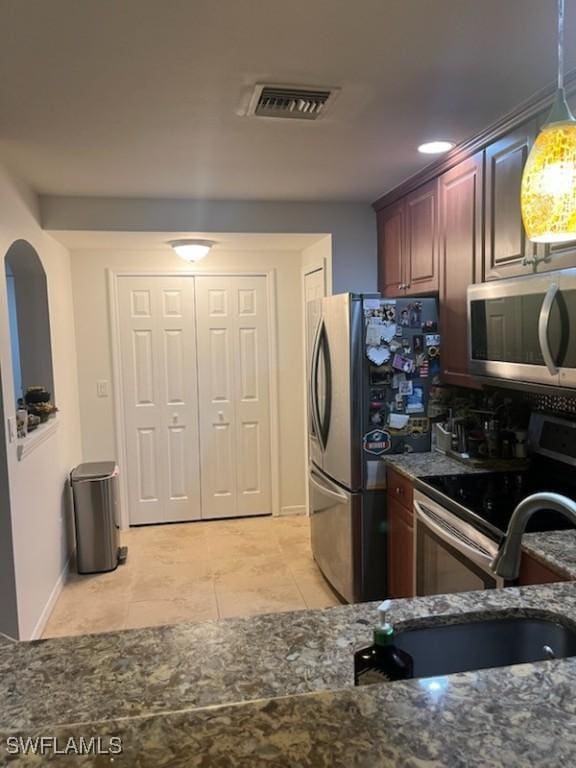 kitchen featuring sink, pendant lighting, dark stone counters, light tile patterned floors, and appliances with stainless steel finishes