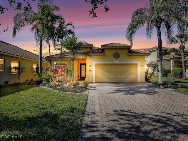 mediterranean / spanish home with a tile roof, stucco siding, a lawn, decorative driveway, and an attached garage