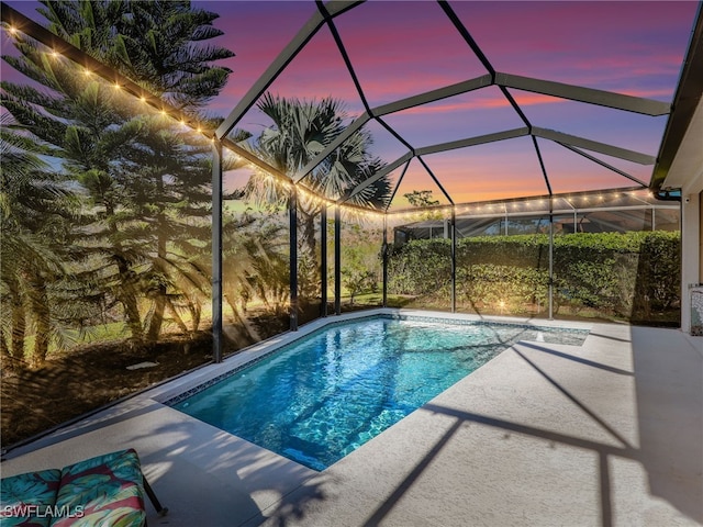 pool at dusk featuring glass enclosure and a patio area