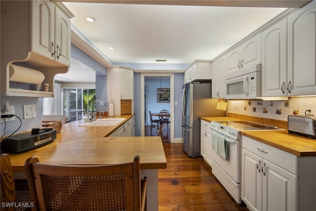 kitchen with butcher block counters, sink, white appliances, and kitchen peninsula