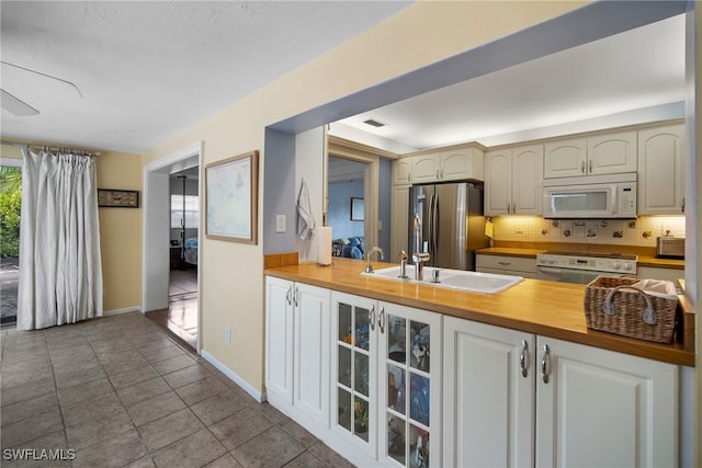 kitchen featuring wood counters, backsplash, white appliances, sink, and light tile patterned floors