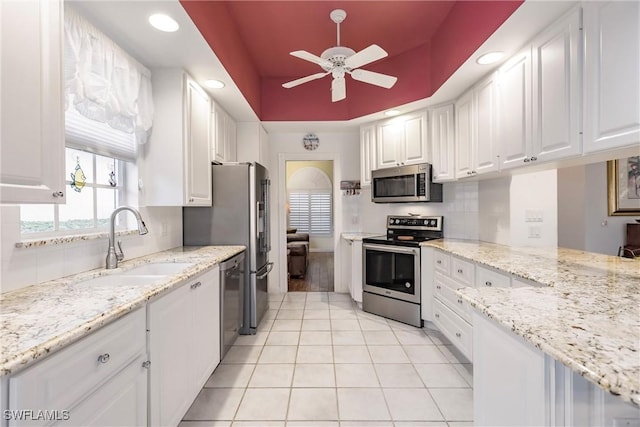 kitchen featuring light stone countertops, white cabinetry, ceiling fan, stainless steel appliances, and a raised ceiling