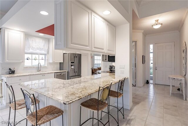 kitchen featuring kitchen peninsula, stainless steel appliances, light stone countertops, white cabinets, and a kitchen breakfast bar