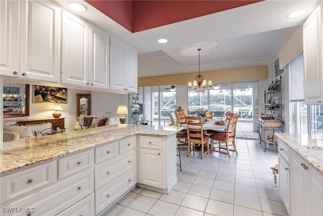 kitchen with white cabinetry, pendant lighting, light stone counters, light tile patterned floors, and ceiling fan with notable chandelier